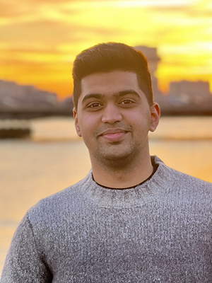 A smiling person with a body of water and a sunset-filled sky behind him