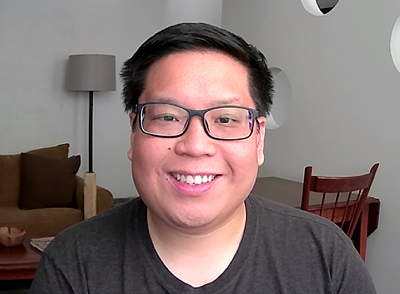 A smiling person indoors with desk and lamp in the background