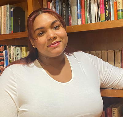 A person smiles with her arm resting on a shelf of the bookcase behind her