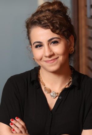 a smiling person in a black shirt and a necklace in an informal setting