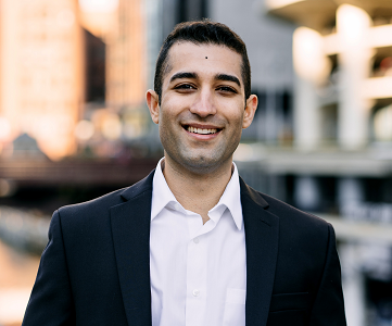 Rouzbeh in a white shirt and dark blazer in front of a blurred urban background