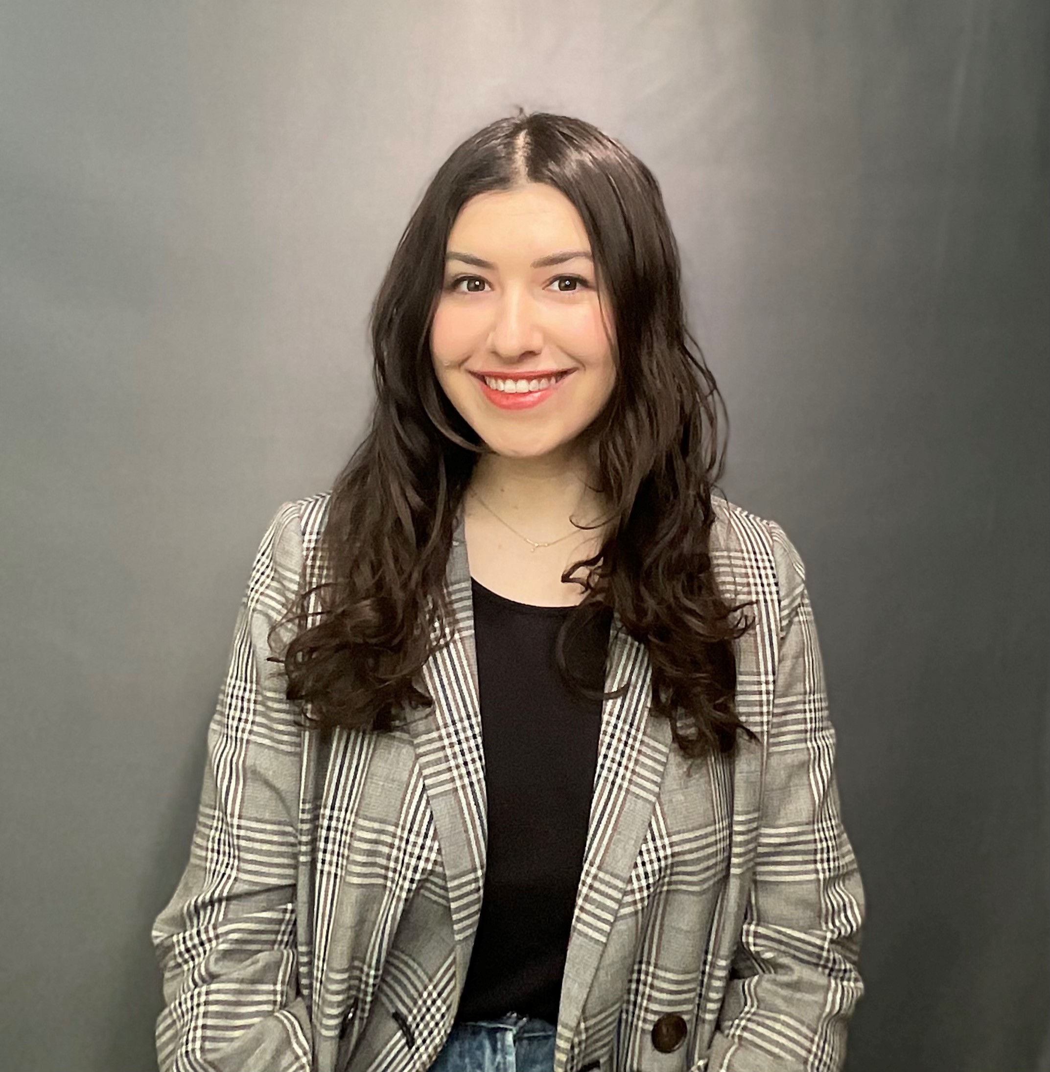 Portrait of a smiling person with long dark hair, wearing a black shirt and gray jacket