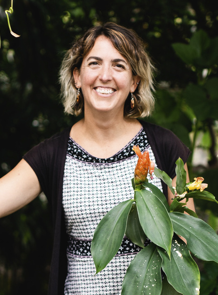 A casual three quarter's picture of Chelsea holding a bouquet in front of a dark background. She is smiling broadly.