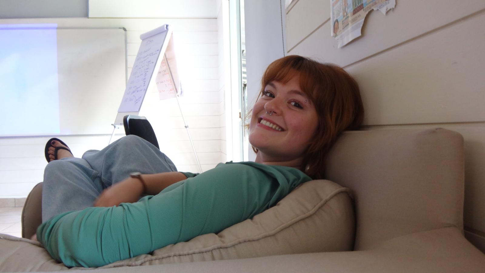 A seated smiling person looks over her shoulder at the camera in an indoor casual setting