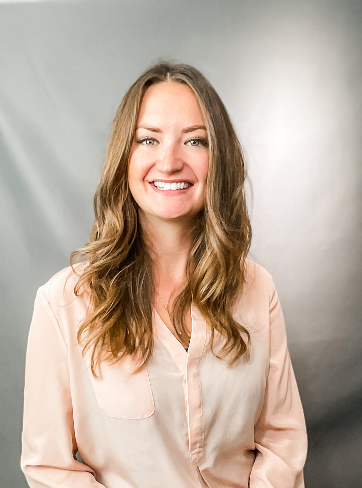 Indoor portrait of Rachel Perry, smiling at the camera in front of a gray fabric backdrop