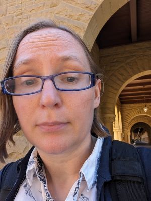 an informal portrait of Courtney Roby wearing glasses in front of an architectural backdrop