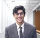 A smiling person wearing a suit and tie in an indoor hallway