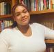 A person smiles with her arm resting on a shelf of the bookcase behind her