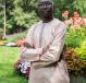 Oumar stands in a garden with his arms crossed. He is looking directly at the camera.