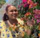 A person stands in a garden next to blooming flowers. She's wearing a floral dress and smiling.