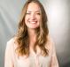 Indoor portrait of Rachel Perry, smiling at the camera in front of a gray fabric backdrop